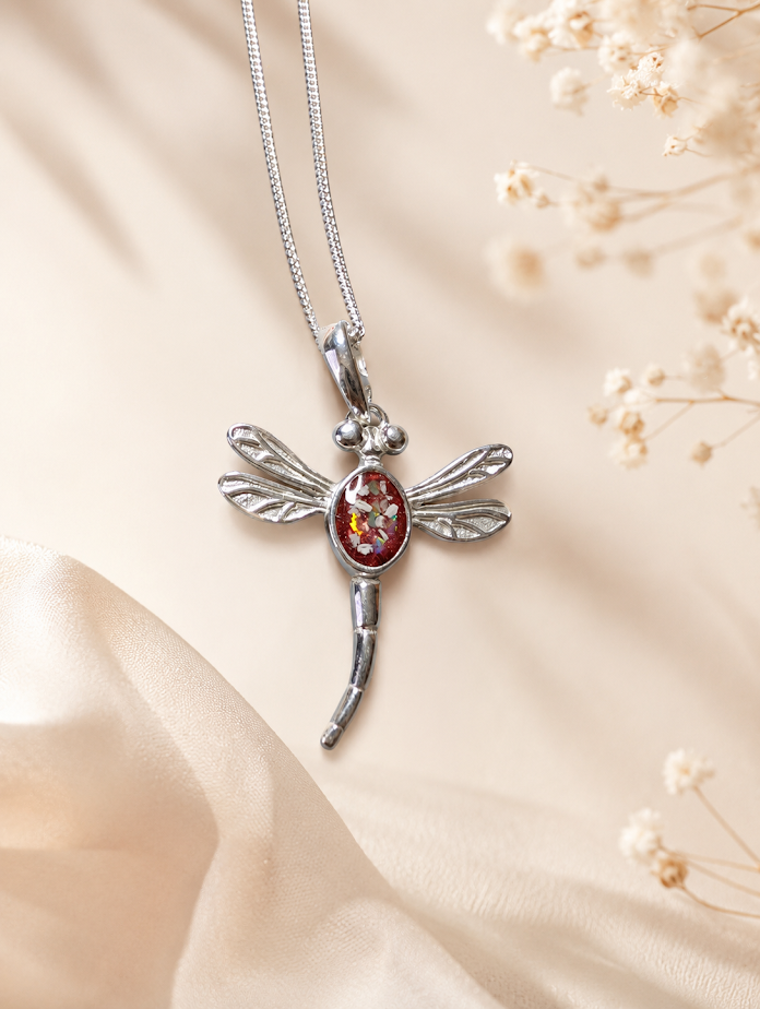 Silver dragonfly pendant with a red gemstone on a delicate chain, against a soft background.