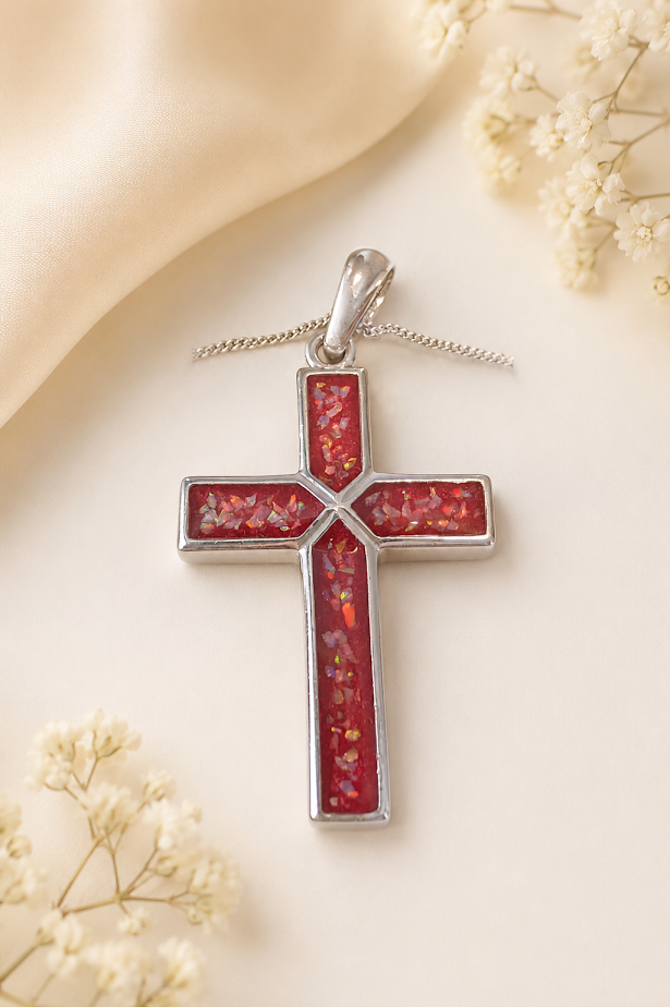 Silver cross pendant with red enamel details on a soft, neutral background.