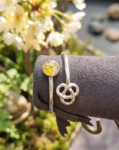 Sterling Silver Knot Memorial ashes, hair or fur Ring Silver bracelets with a yellow gemstone and a knot design, displayed with flowers in background.